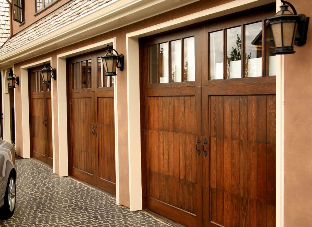 Elegant wooden garage doors with windows, complemented by vintage-style lanterns.