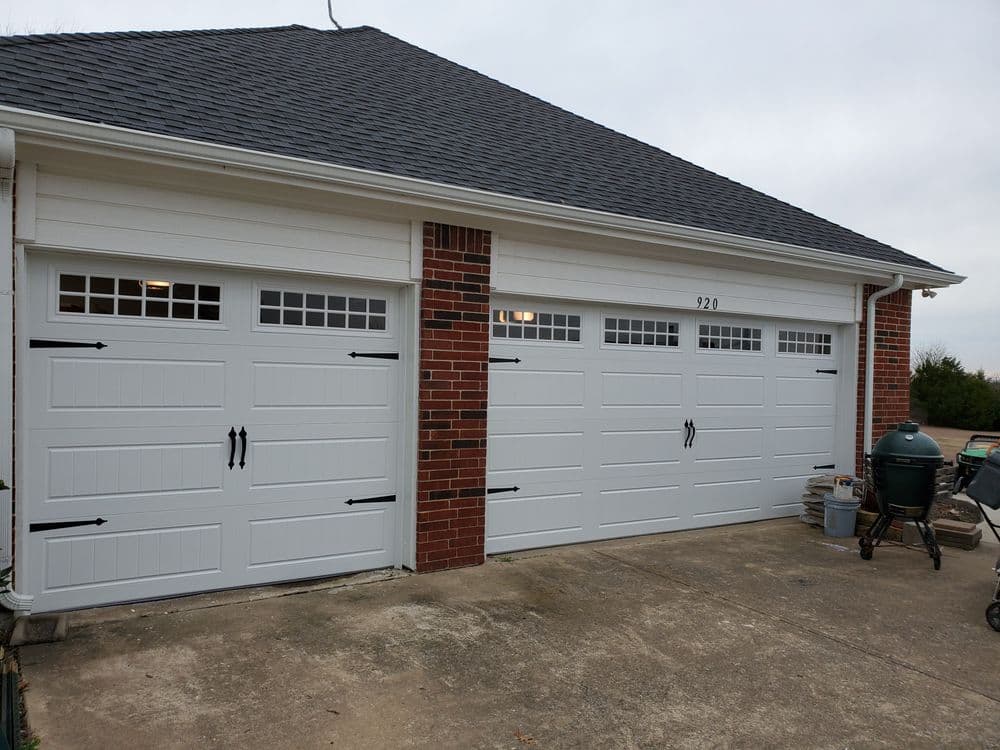 White three-car garage doors with decorative hardware and brick accents on a residential property.
