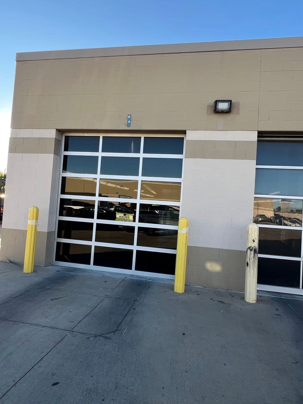 Commercial building entrance with large glass doors and yellow bollards in front.