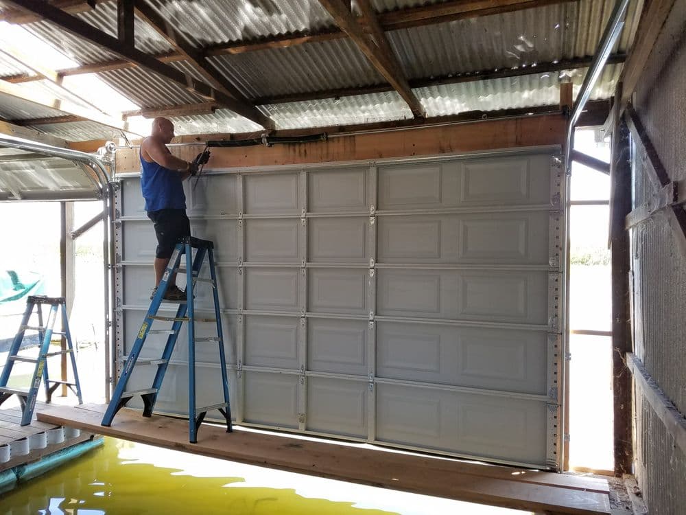 Man installing a garage door while standing on a ladder in a workshop.