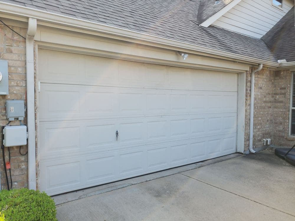 Residential garage door on a brick house with a clean driveway and exterior lighting.
