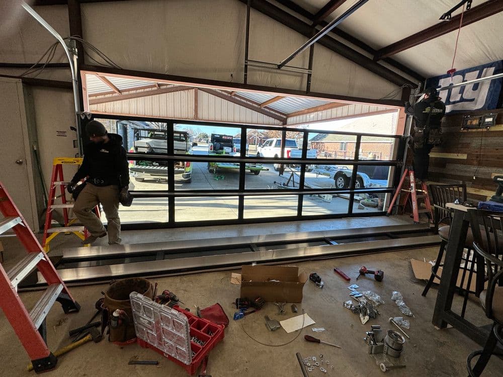 Garage door installation in a workshop with tools and a ladder visible.