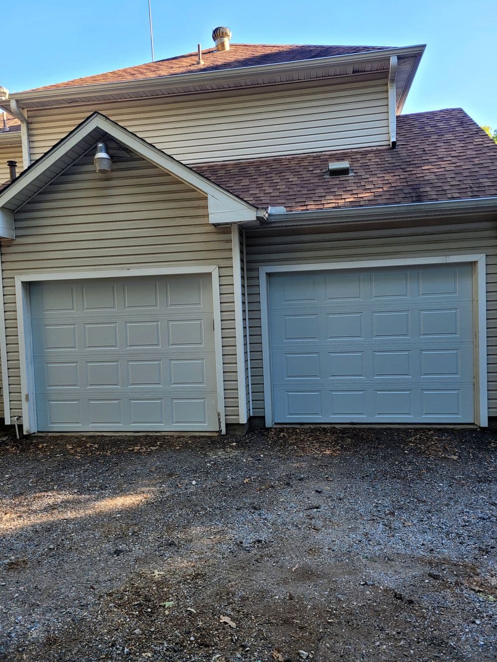 Two light blue garage doors on a beige house with a gravel driveway.