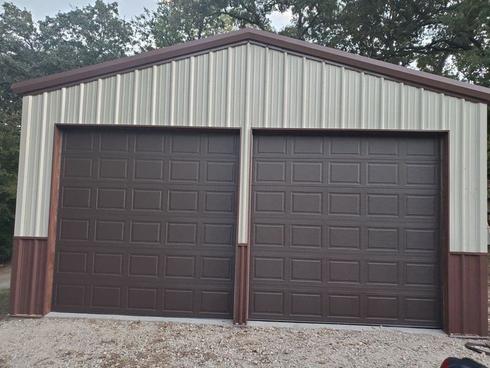 Metal storage building with two brown garage doors and a gray gravel driveway.