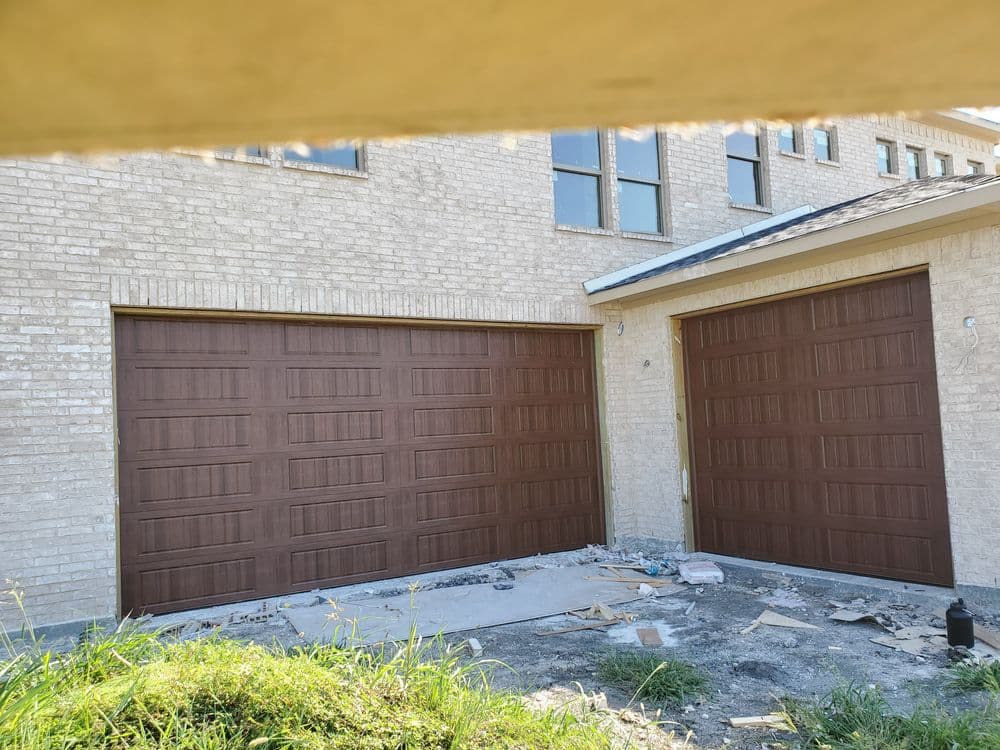 Newly installed brown garage doors on a modern brick home with construction debris nearby.