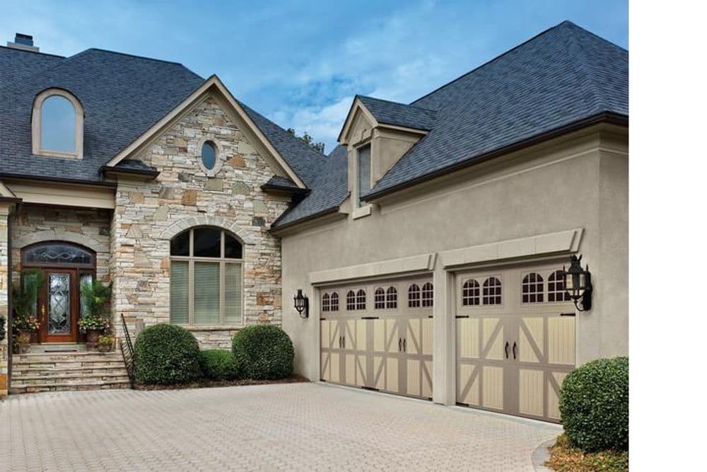 Elegant stone and stucco home with double garage and landscaped driveway under blue sky.