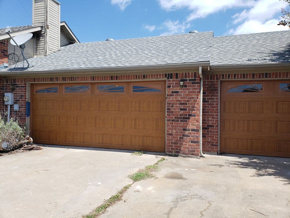 Two large wooden garage doors with diagonal windows on a brick home exterior.