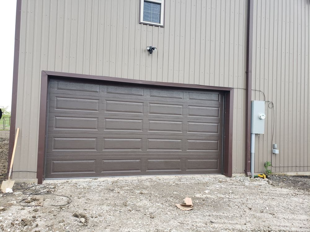 Modern brown garage door on a metal building with electrical panel nearby.