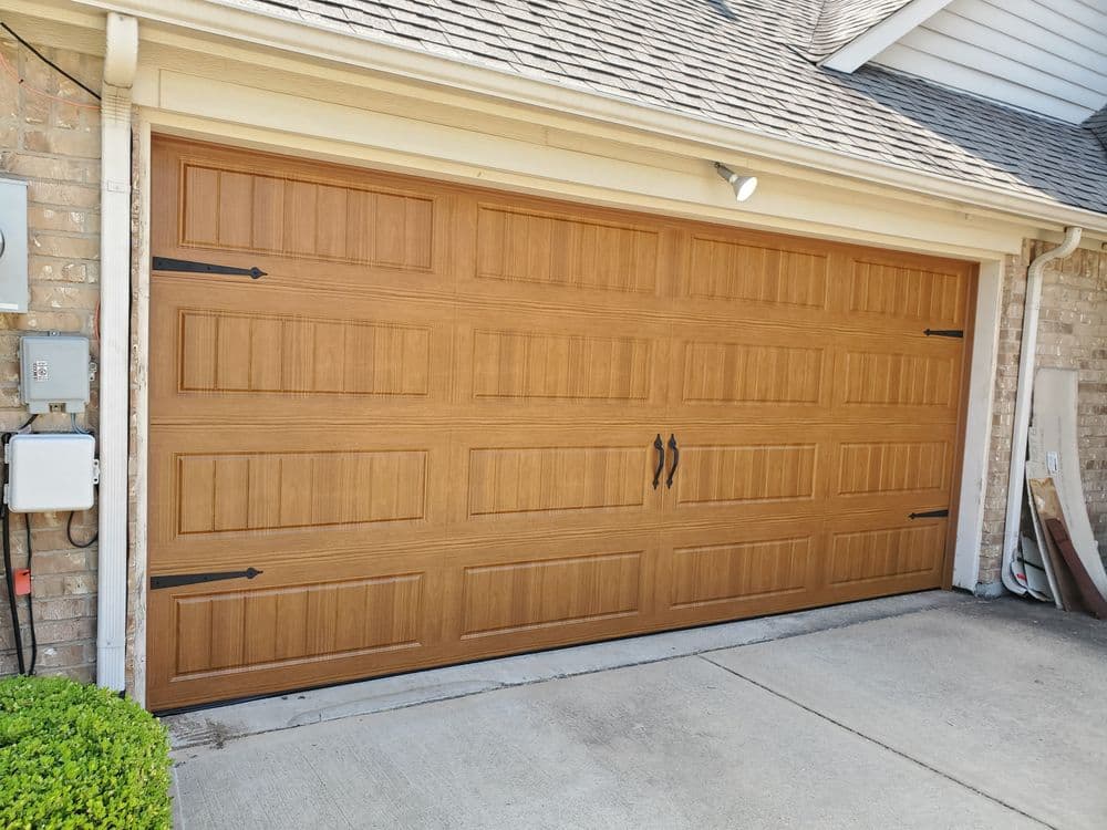 Wooden garage door with horizontal panels, decorative handles, and brick home exterior.