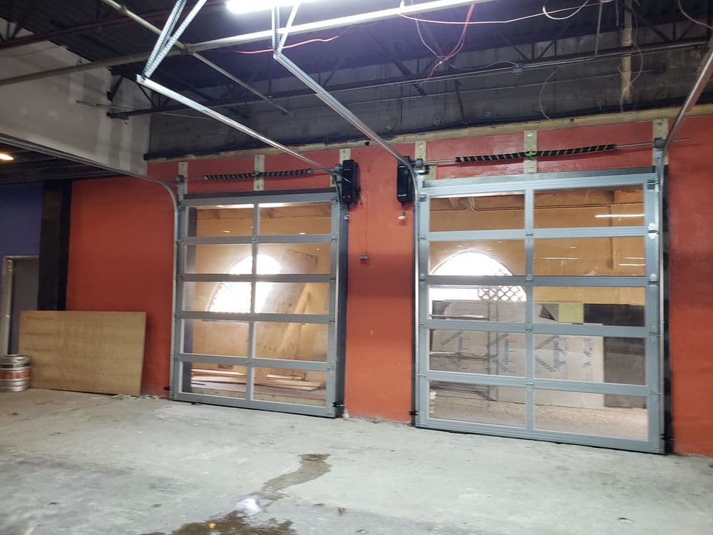 Industrial garage with large glass doors and unfinished interior space, featuring exposed beams.