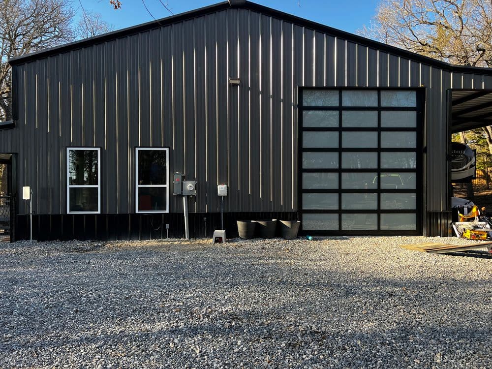 Modern black metal building with large glass garage door and gravel driveway.
