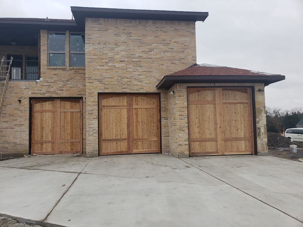 Wooden garage doors on a new brick home with a modern design and concrete driveway.